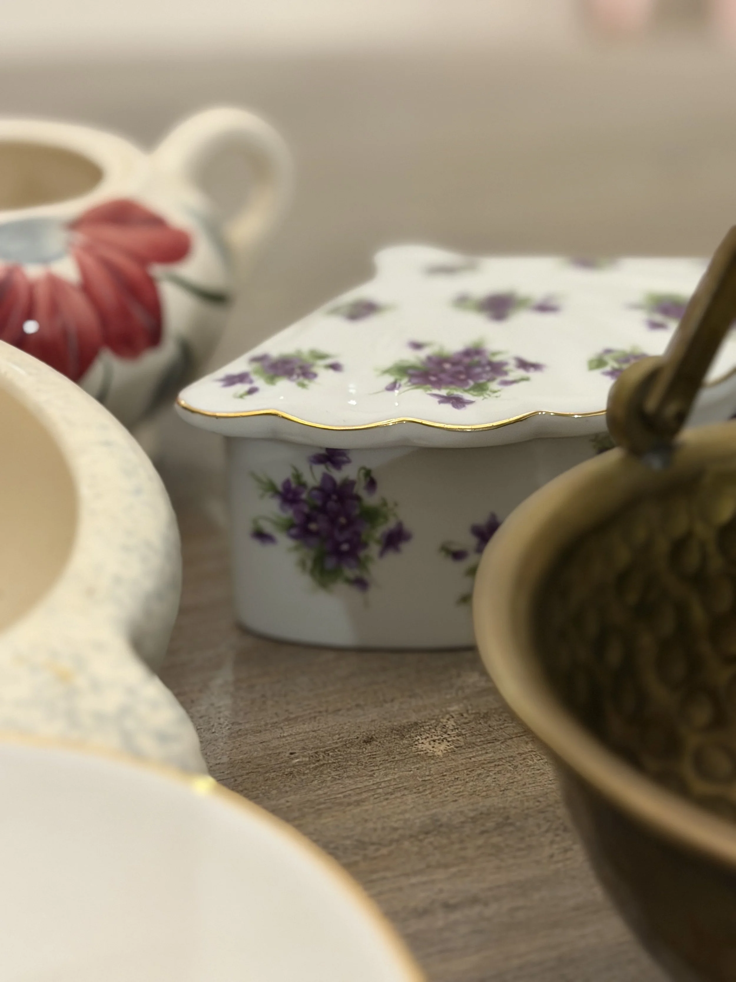 Close-up of floral patterned porcelain container and cups, with a wooden surface and blurred background.