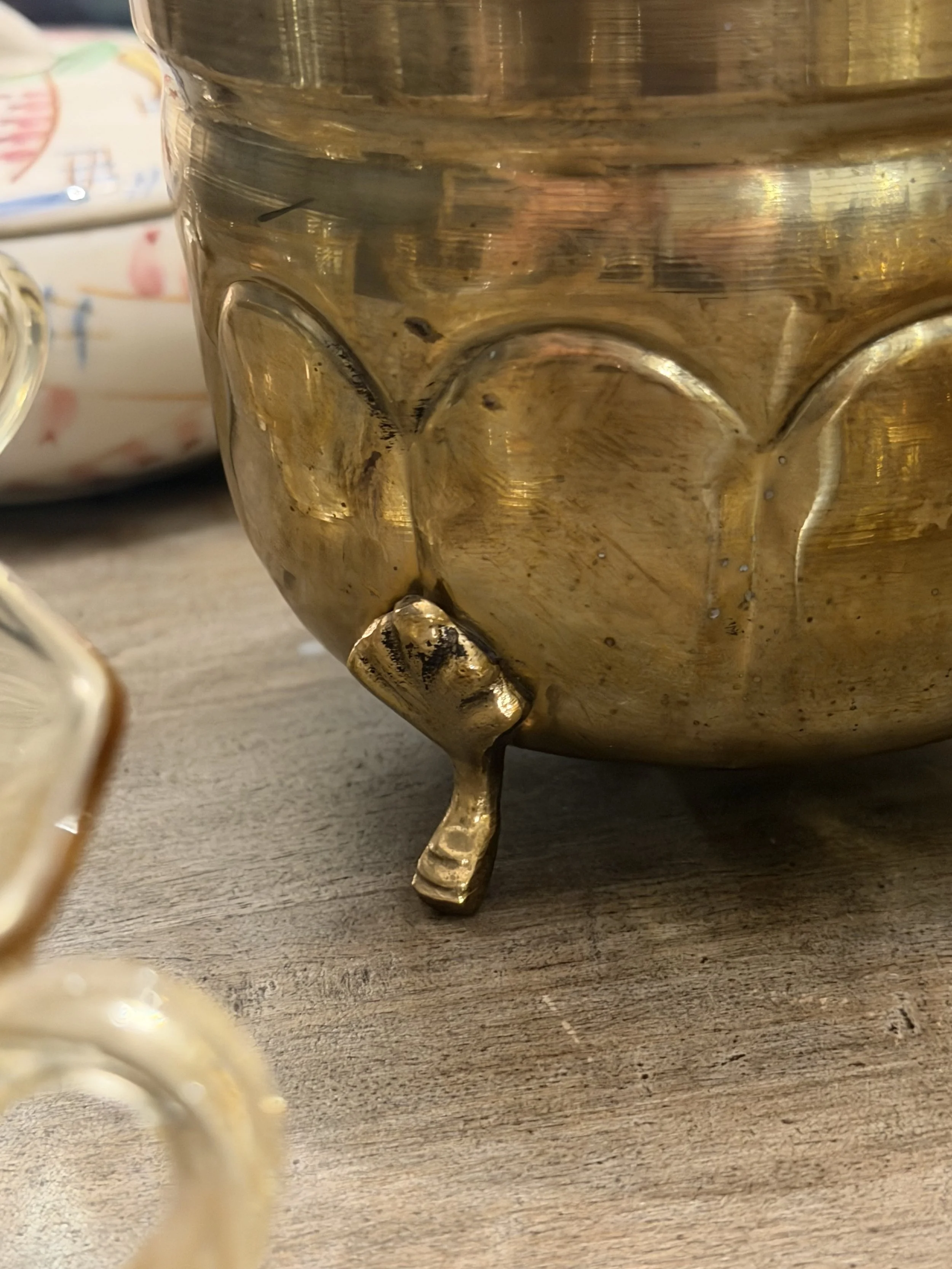 Close-up of a gold-colored mug with a cat face design, showing the top and tail at the bottom, placed on a wooden surface.