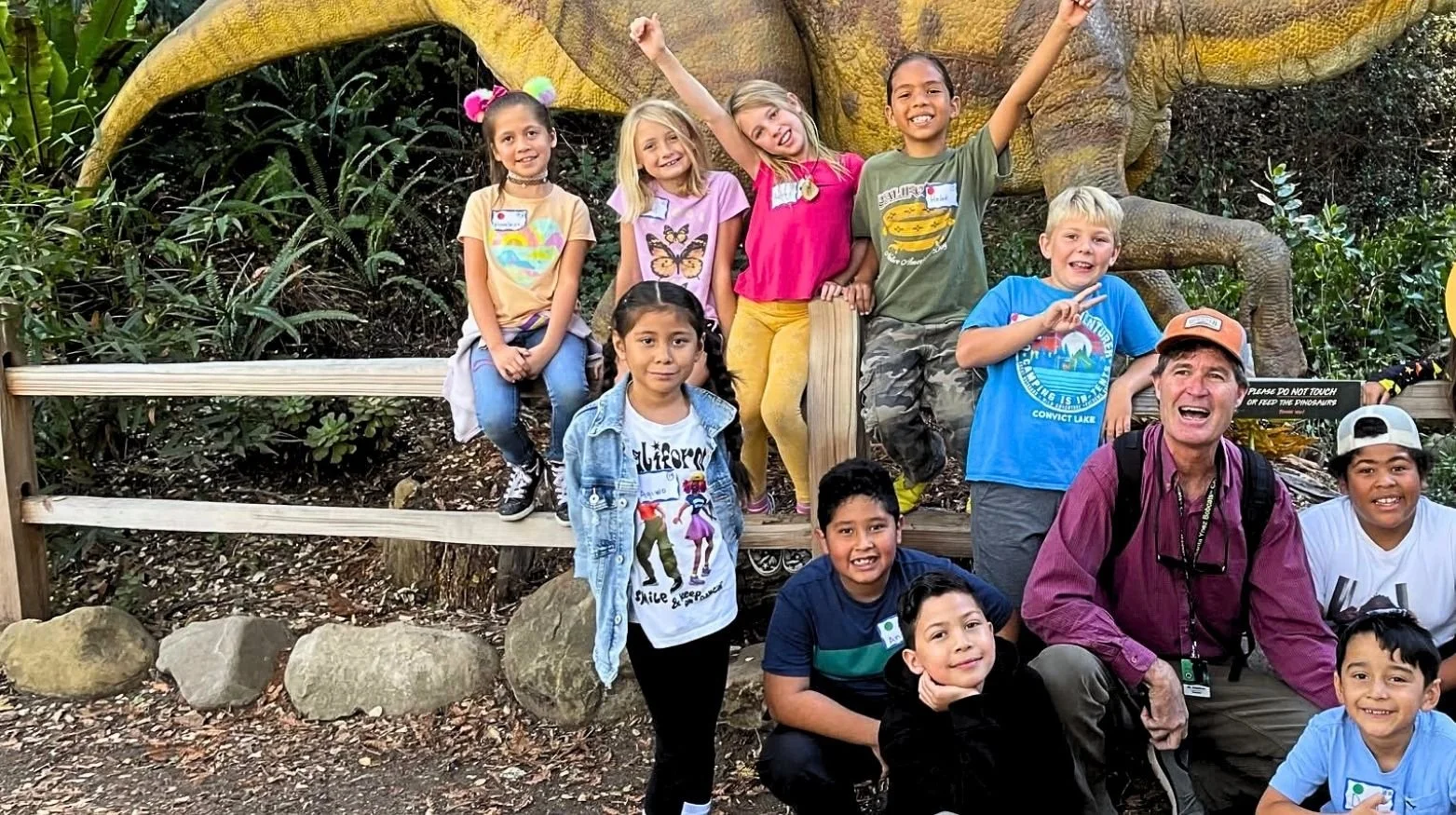 Children and their teacher posing in front of a dinosaur statue while on a field trip.