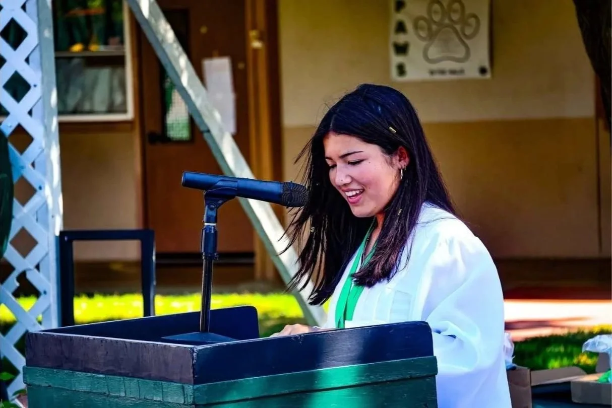 Young woman with dark hair smiling while speaking into a microphone at the Santa Ynez Elementary School 8th Grade Graduation ceremony.