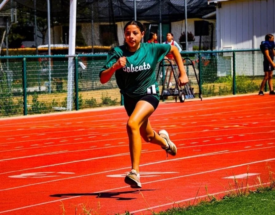 Young female athlete running on a red track during a sports event, wearing a green shirt with
