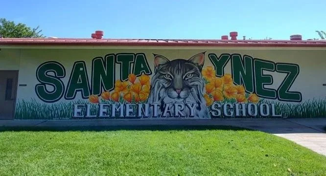 Colorful mural of a jungle cat with yellow flowers and green grass on the wall of Santa Ynez Elementary School.