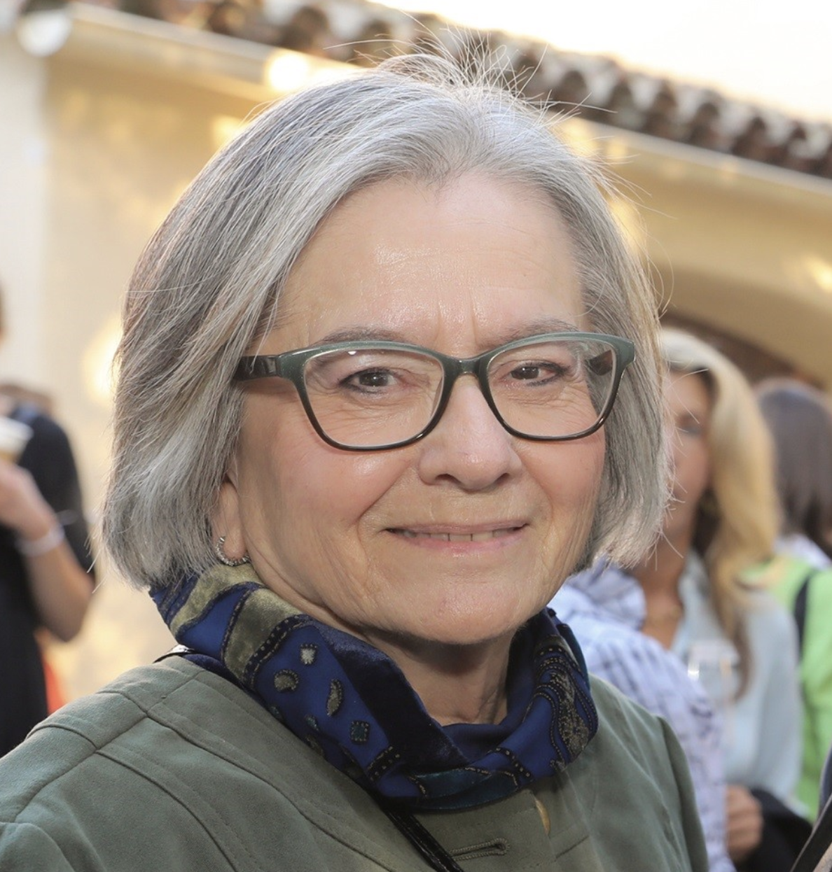 Photo of board trustee member, Molly Carrillo-Walker, wearing a scarf, smiling outdoors at sunset.
