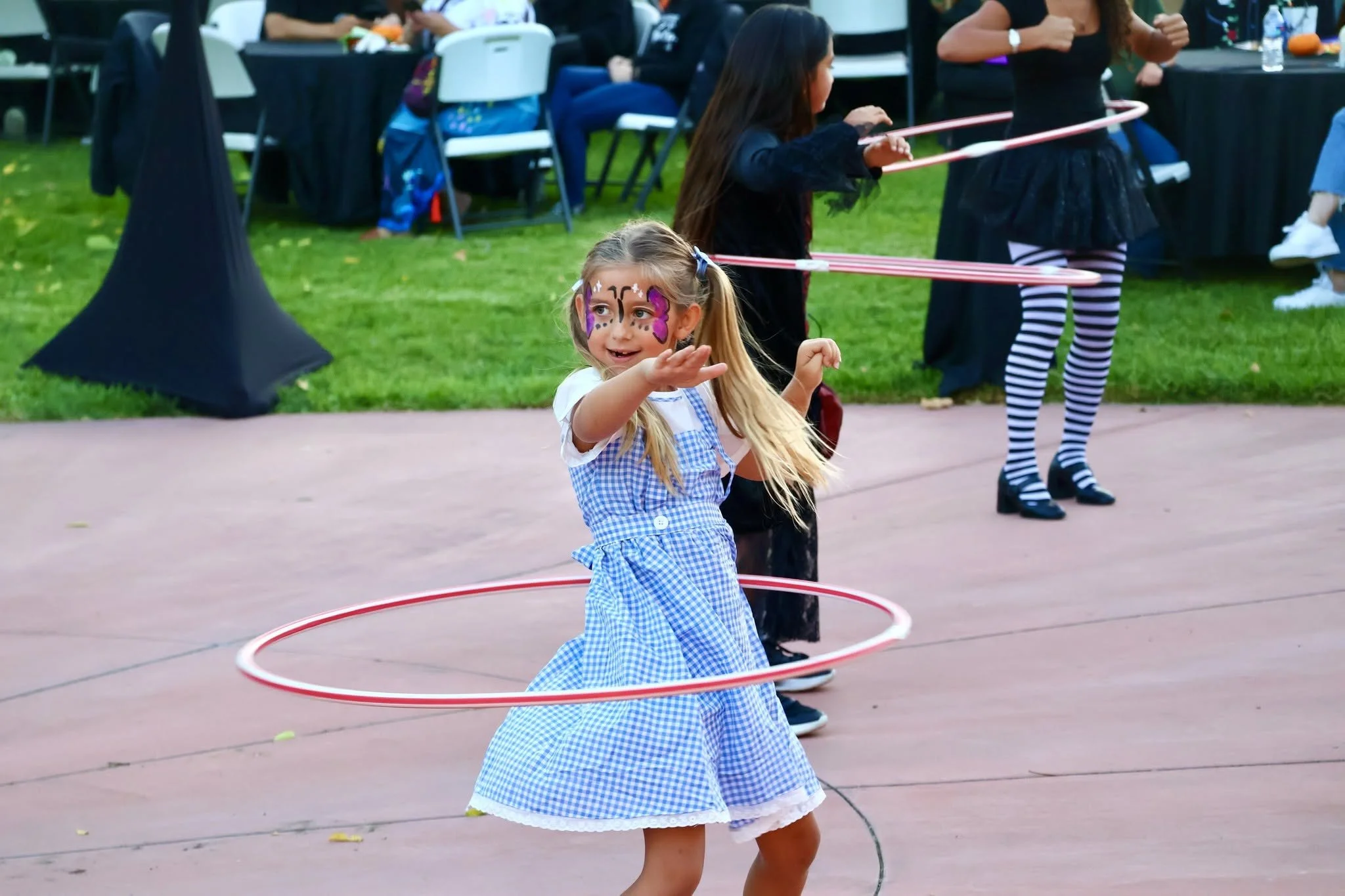 Young girl with butterfly face paint playing with a hula hoop at an outdoor event.