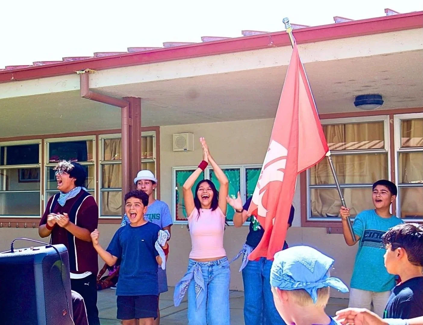 Children celebrating with a flag outside a school building.
