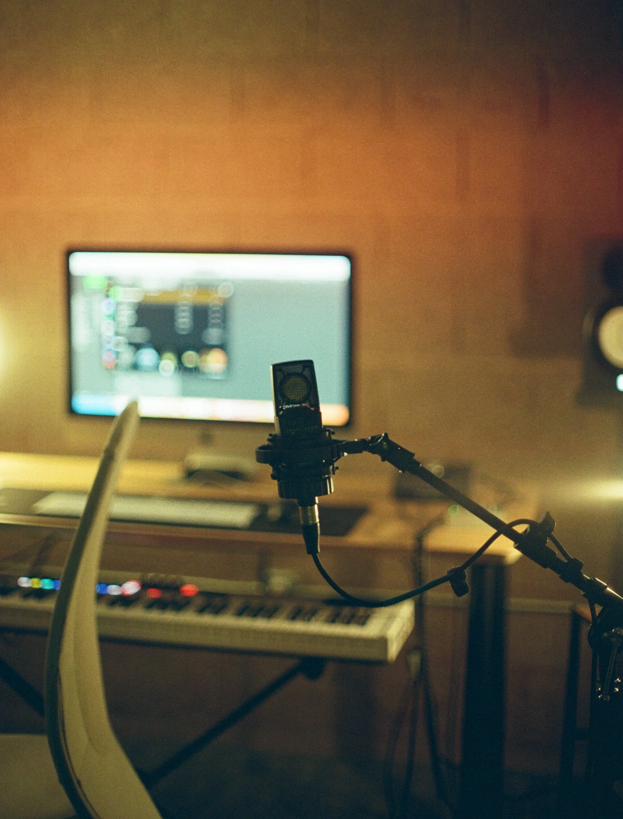 A computer monitor on a desk displaying a digital audio workstation with a microphone and cables in the foreground in a dimly lit room.