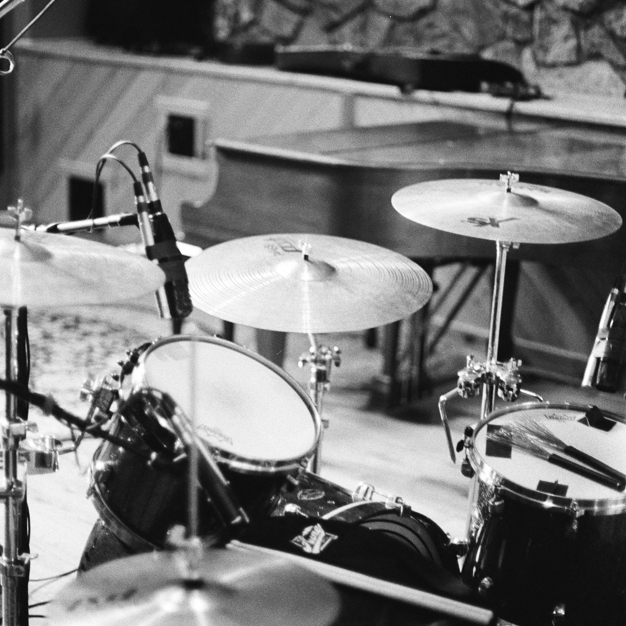 Close-up of a drum set, focusing on the cymbals and part of the drum kit, with a background of a stone wall.
