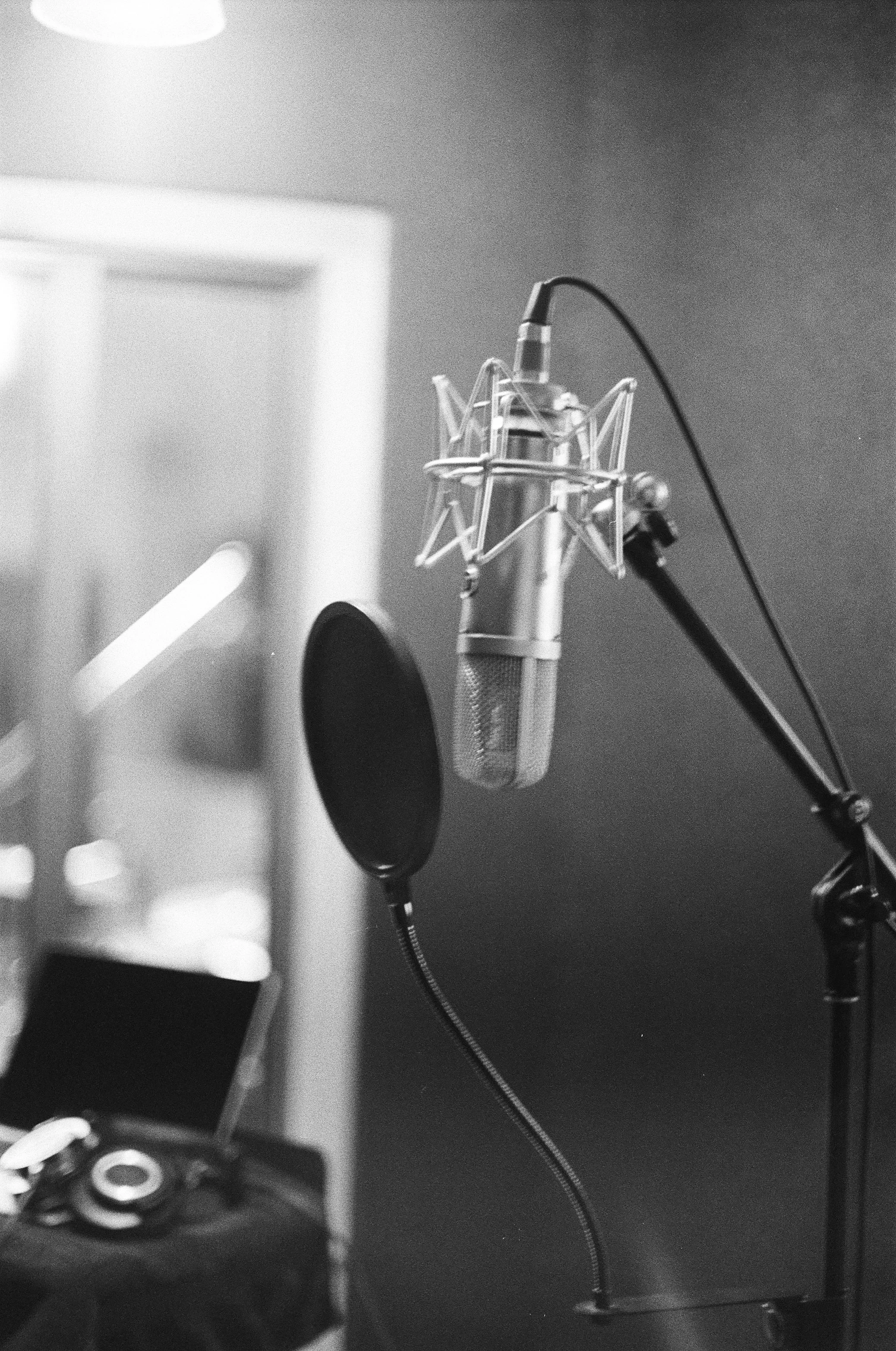 Close-up of a professional studio condenser microphone on a boom arm with a pop filter in a recording studio, with a blurred background.