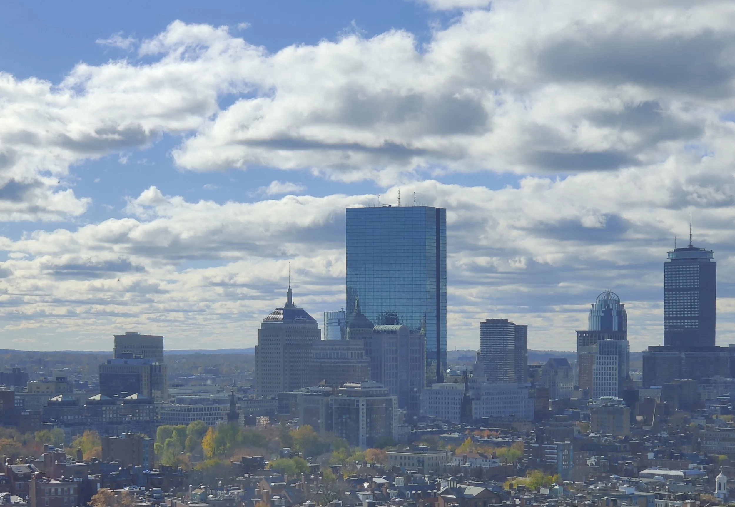 Boston city skyline with tall skyscrapers under partly cloudy sky.