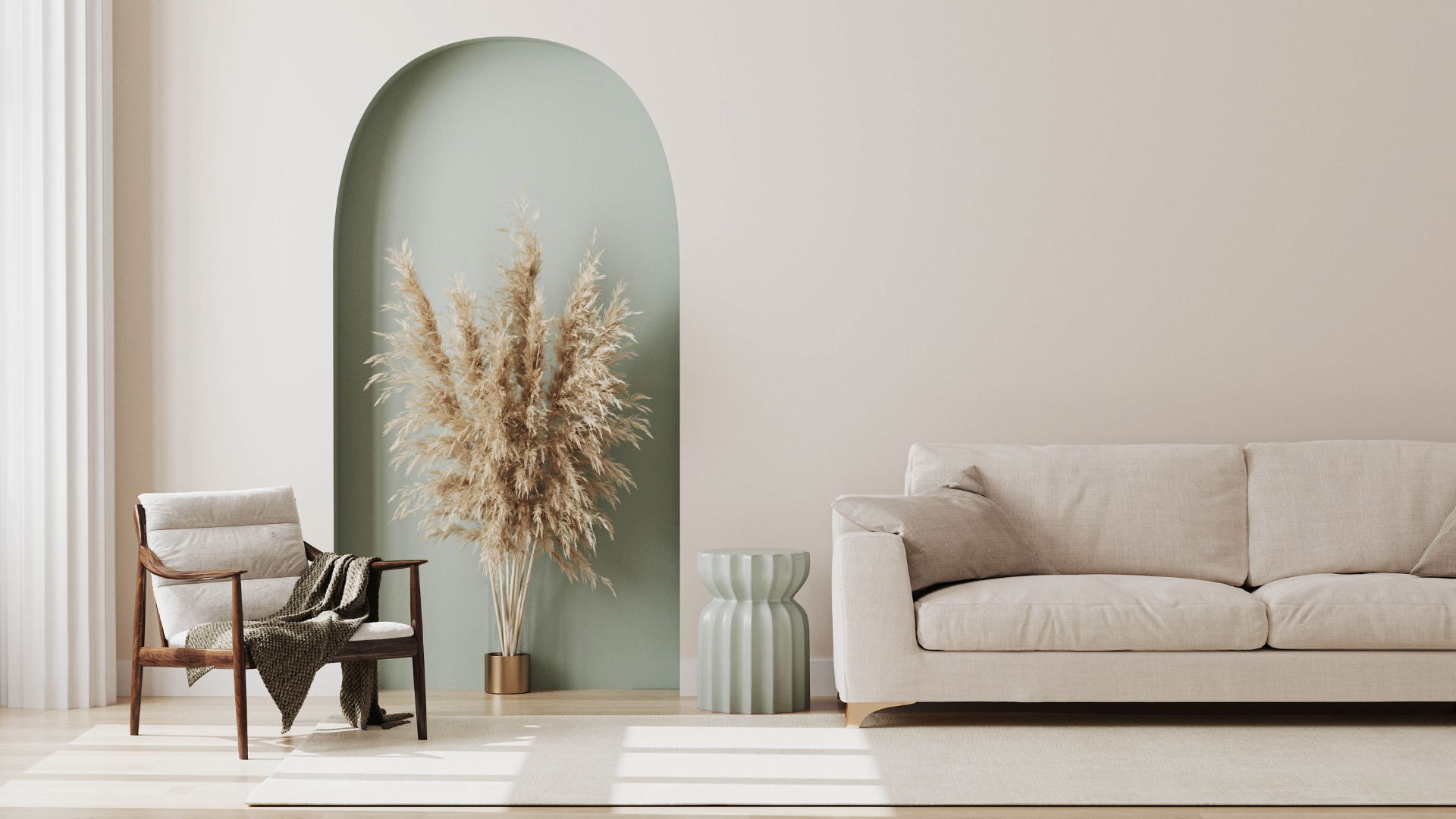 Minimalist living room with a beige sofa, a chair with a blanket, and dried pampas grass in a gold vase, against a light wall with an arched green accent and natural light.