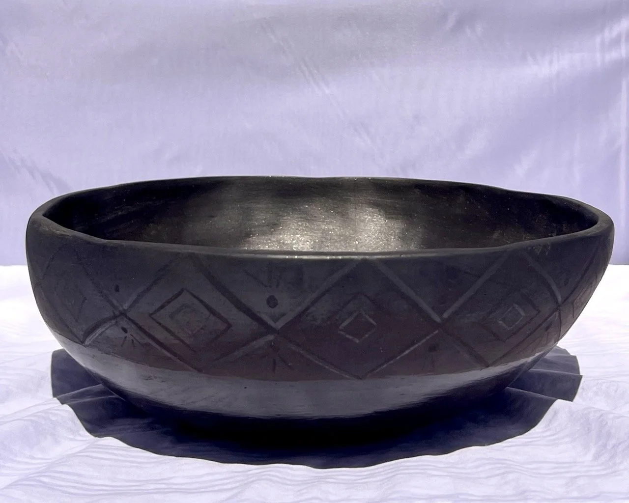 Black carved bowl with geometric patterns on a white surface.