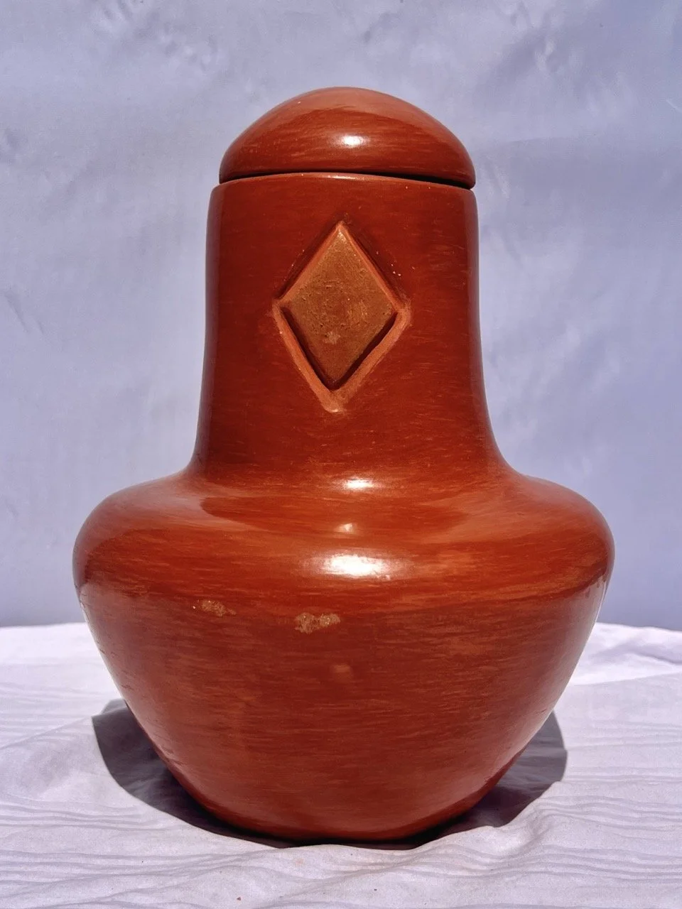 A wooden vase with a rounded, bulbous base, a narrow neck, and a rounded lid. The vase has a diamond-shaped carving on the front.