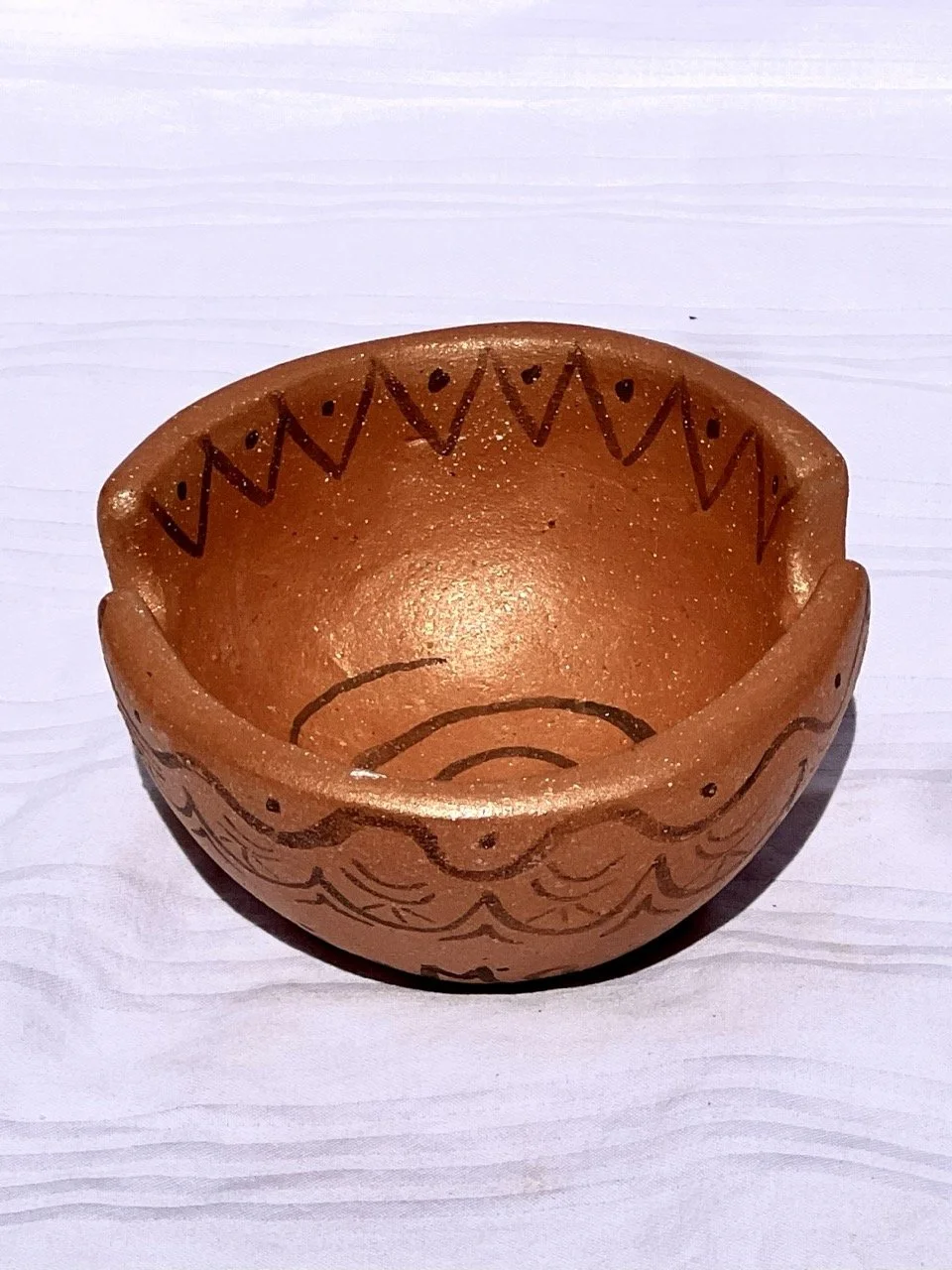 A small, round terracotta bowl with black decorative patterns on the inside and outside, placed on a white wooden surface.