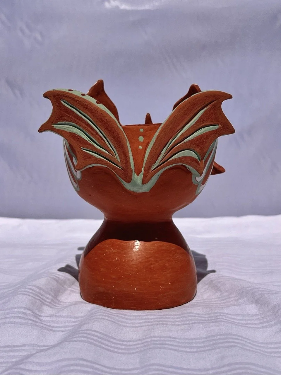 Decorative ceramic bowl with orange, white, and green details, shaped like a blooming flower, placed on a white surface with a plain background.