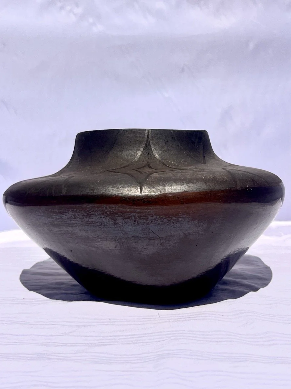 A black ceramic vase with a wide, rounded body and narrow opening on a white surface, casting a shadow.