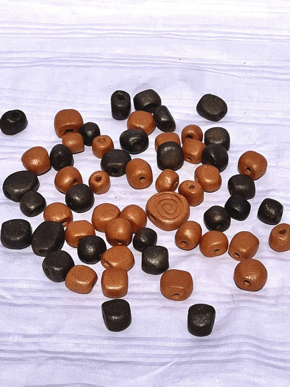 A collection of small, round beads in black and brown colors scattered on a white textured surface.