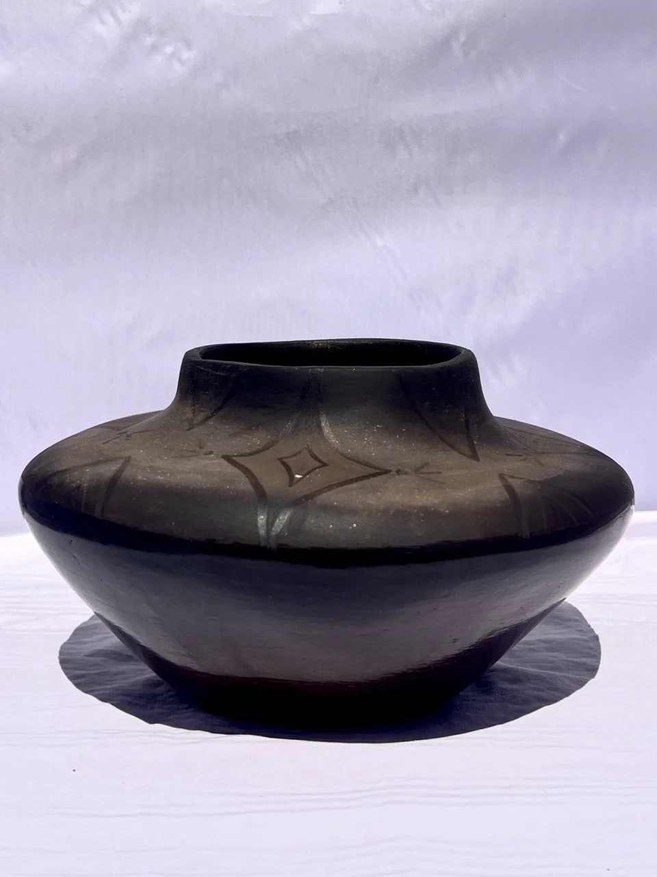 Black pottery jar with geometric designs, placed on a white surface with a light background.