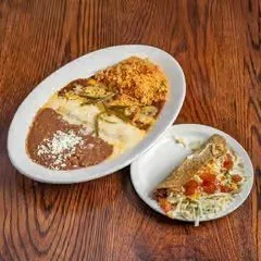 Plate with traditional Mexican food including tacos and a bowl of chili with cheese and toppings on a wooden table.