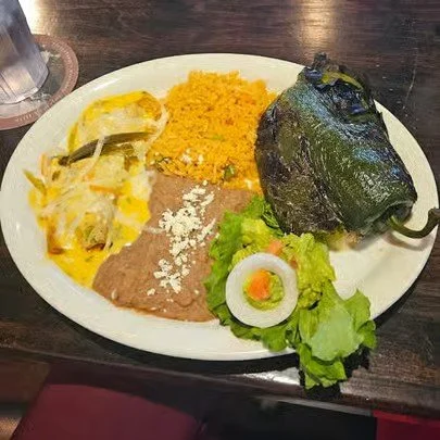 Plate of Mexican food including stuffed jalapeño, yellow rice, refried beans, Mexican taco salad, lettuce, tomato, onion, and a glass of water.