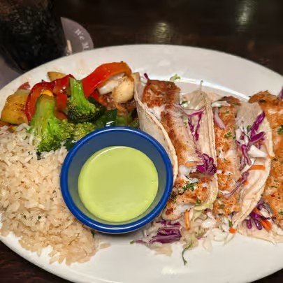 Plate with grilled fish, rice, steamed broccoli, and a small bowl of green sauce