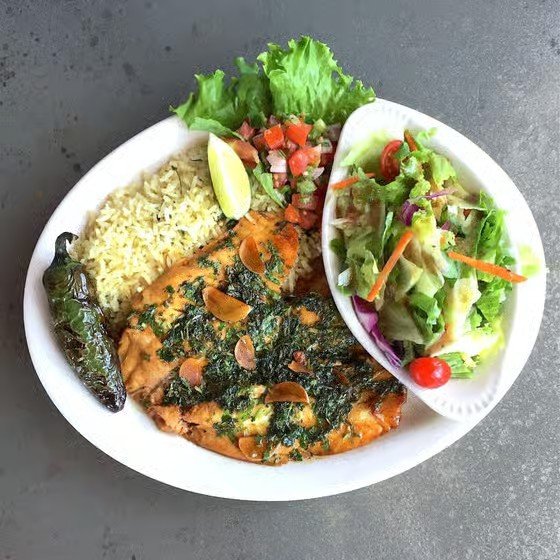 Plate of Mexican food with rice, grilled chicken with herbs, salad with lettuce, tomato, and carrots, and a lime wedge.