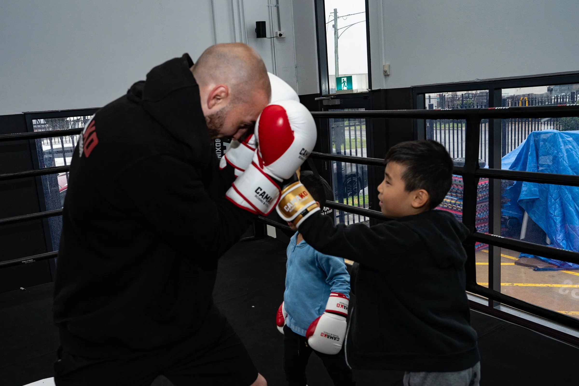 A man and a young boy in boxers and gloves, in a boxing gym, practicing boxing with the man coaching the boy.