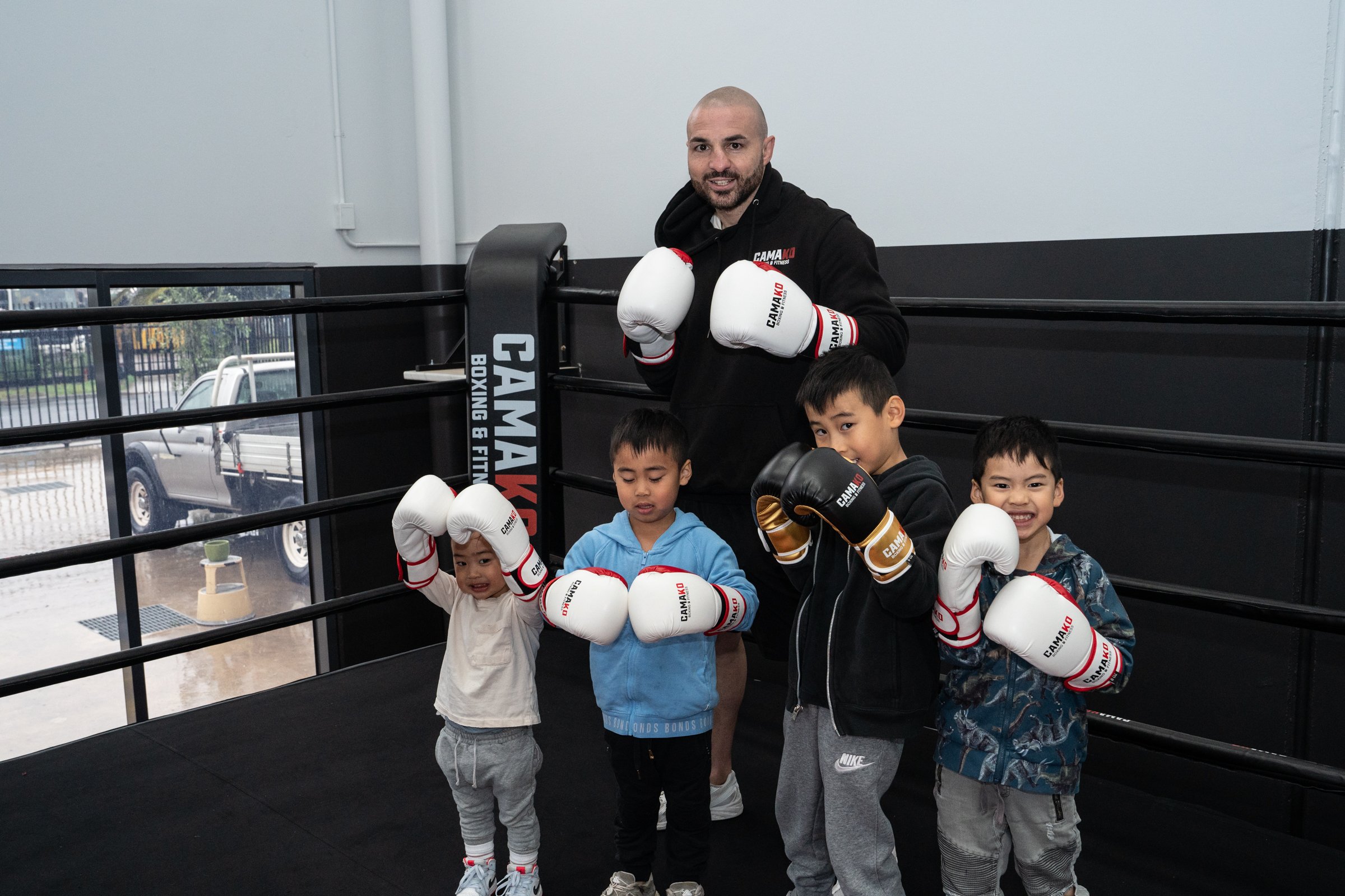 A trainer with boxing gloves and four children in a boxing gym posing for a photo.
