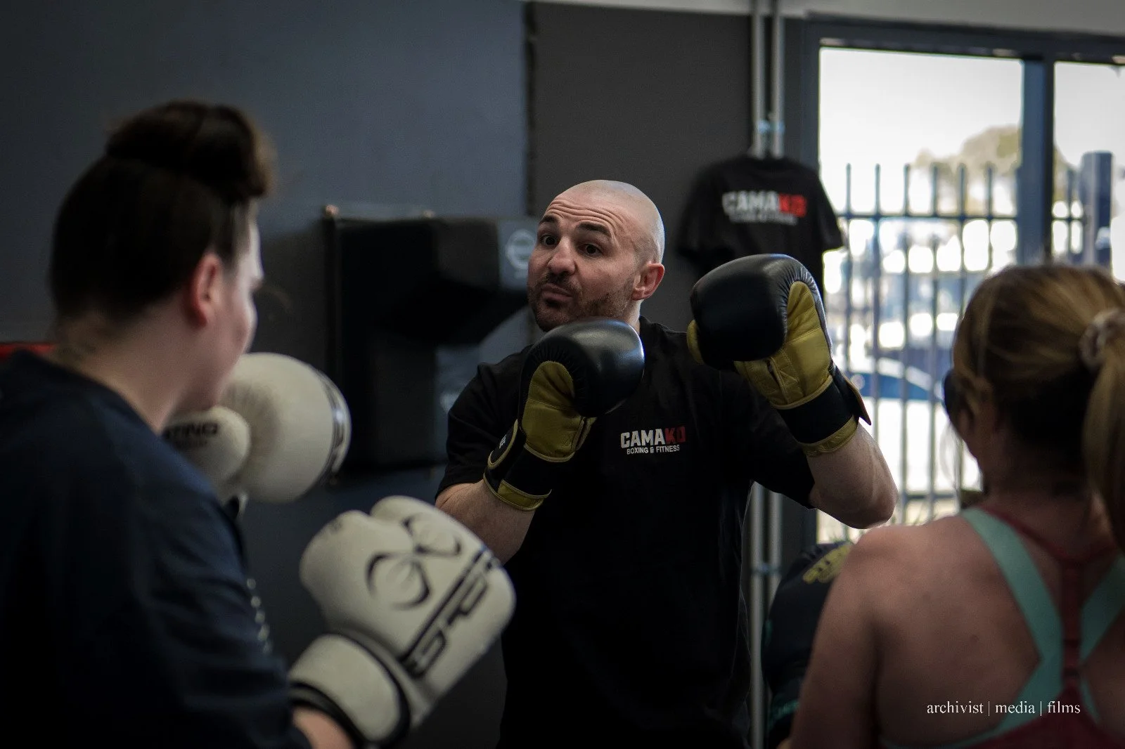 Boxing instructor demonstrating techniques to two women students in a gym.