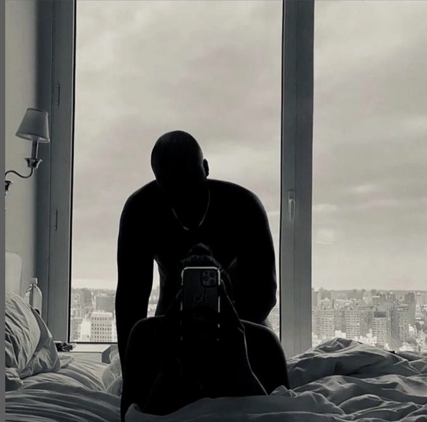 Two people in silhouette on a bed against a window