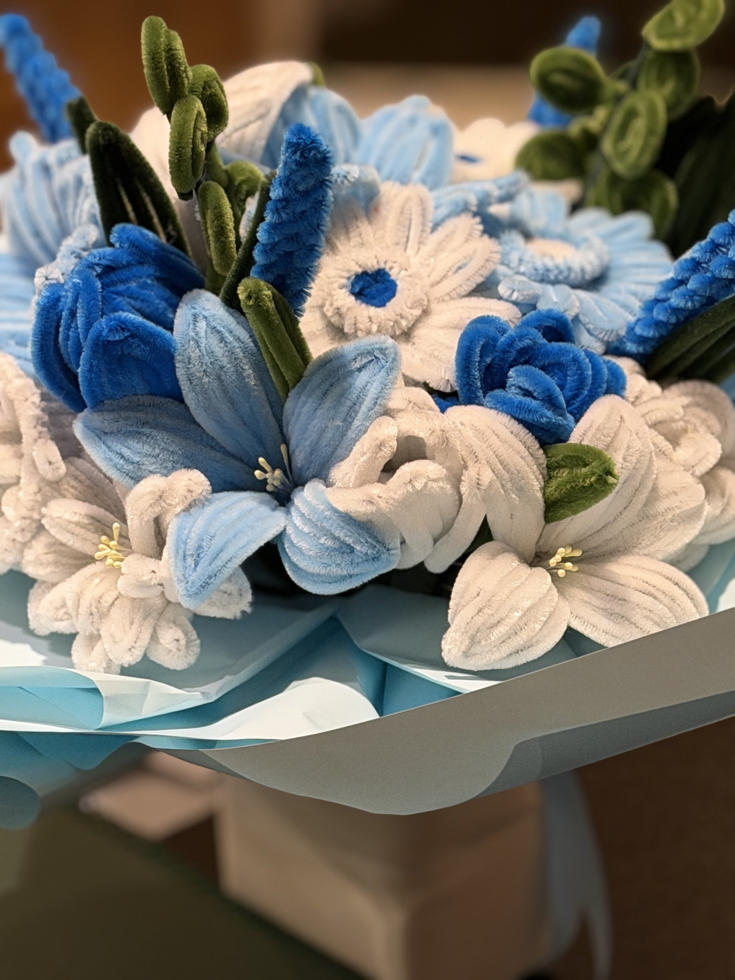 A bouquet of various plush animal toys and flowers in shades of blue and white, wrapped in light blue paper.