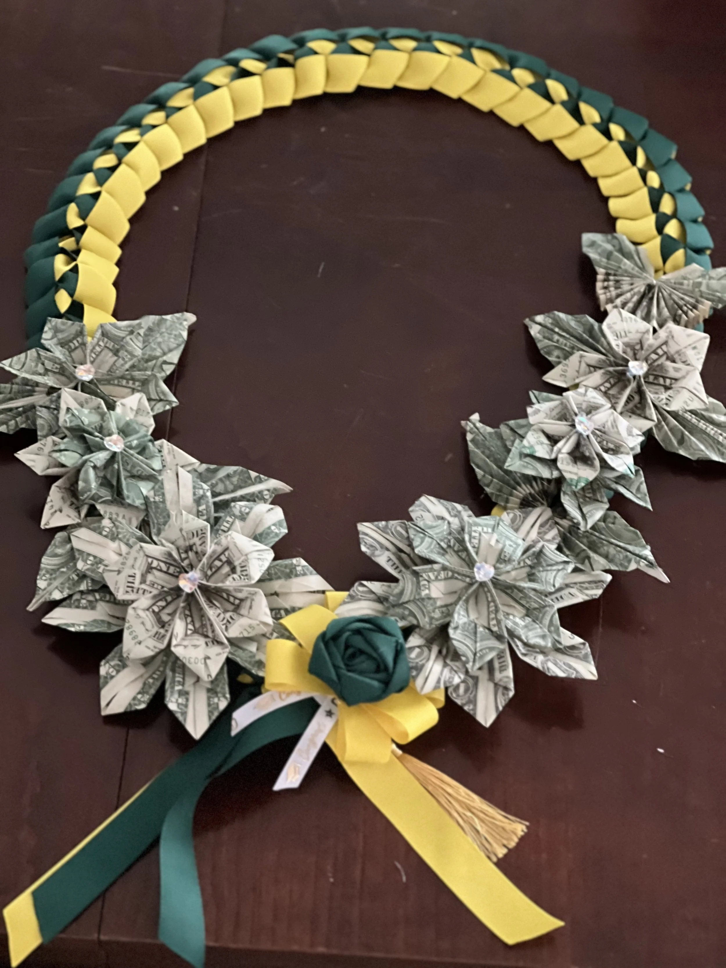 A decorative wreath made from folded dollar bills with paper flowers and ribbons, featuring green and yellow colors.