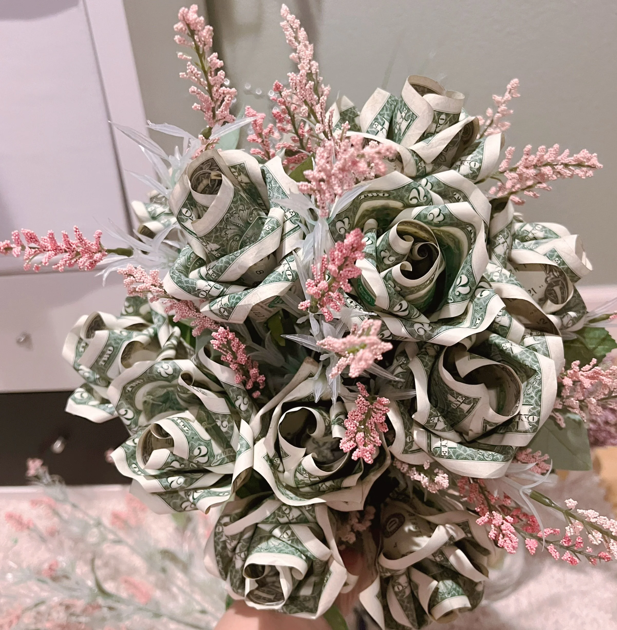 Arrangement of pink artificial flowers intertwined with rolled dollar bills.