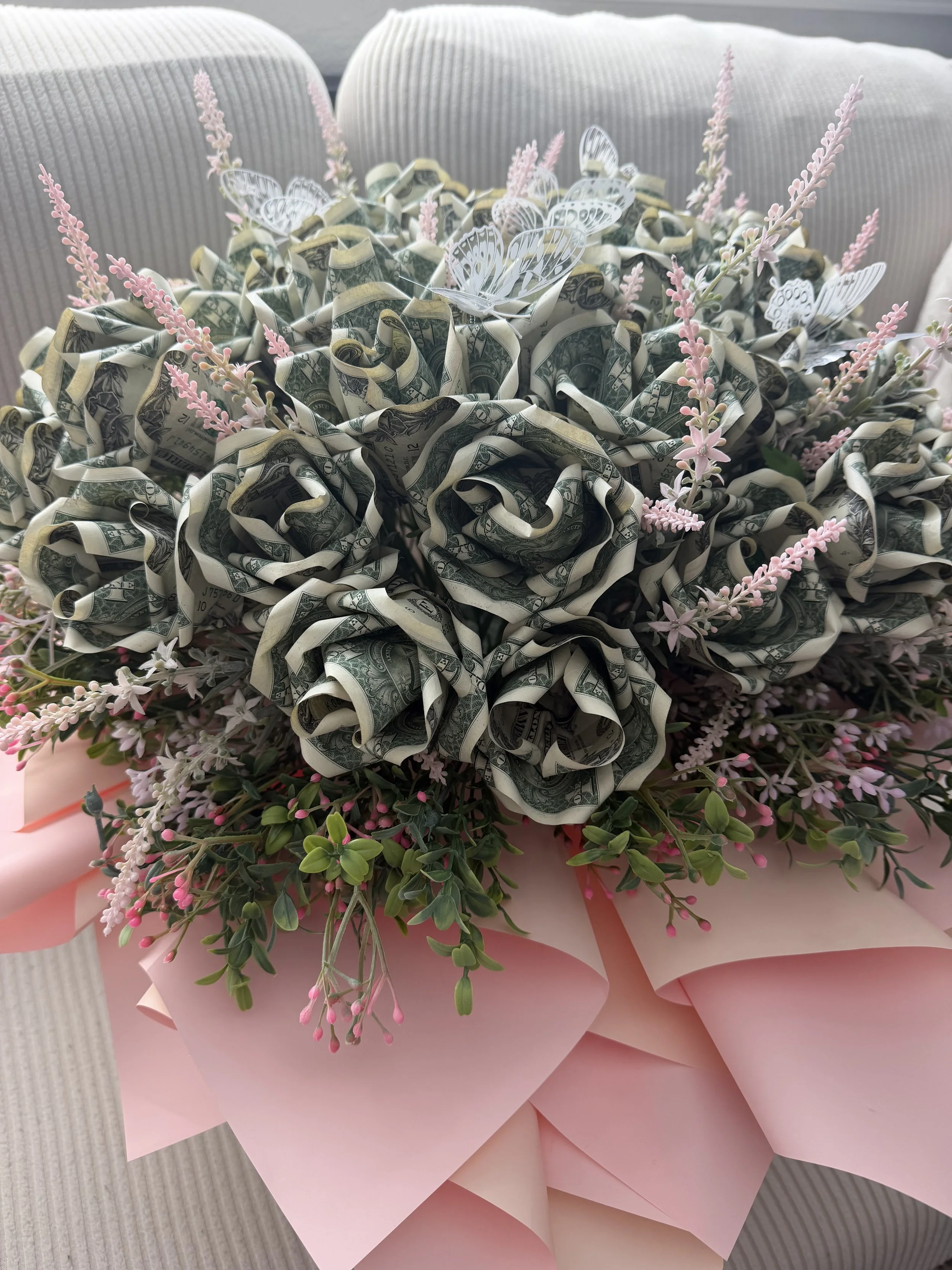 A bouquet made of money, pink flowers, and white butterfly decorations wrapped in pink paper.