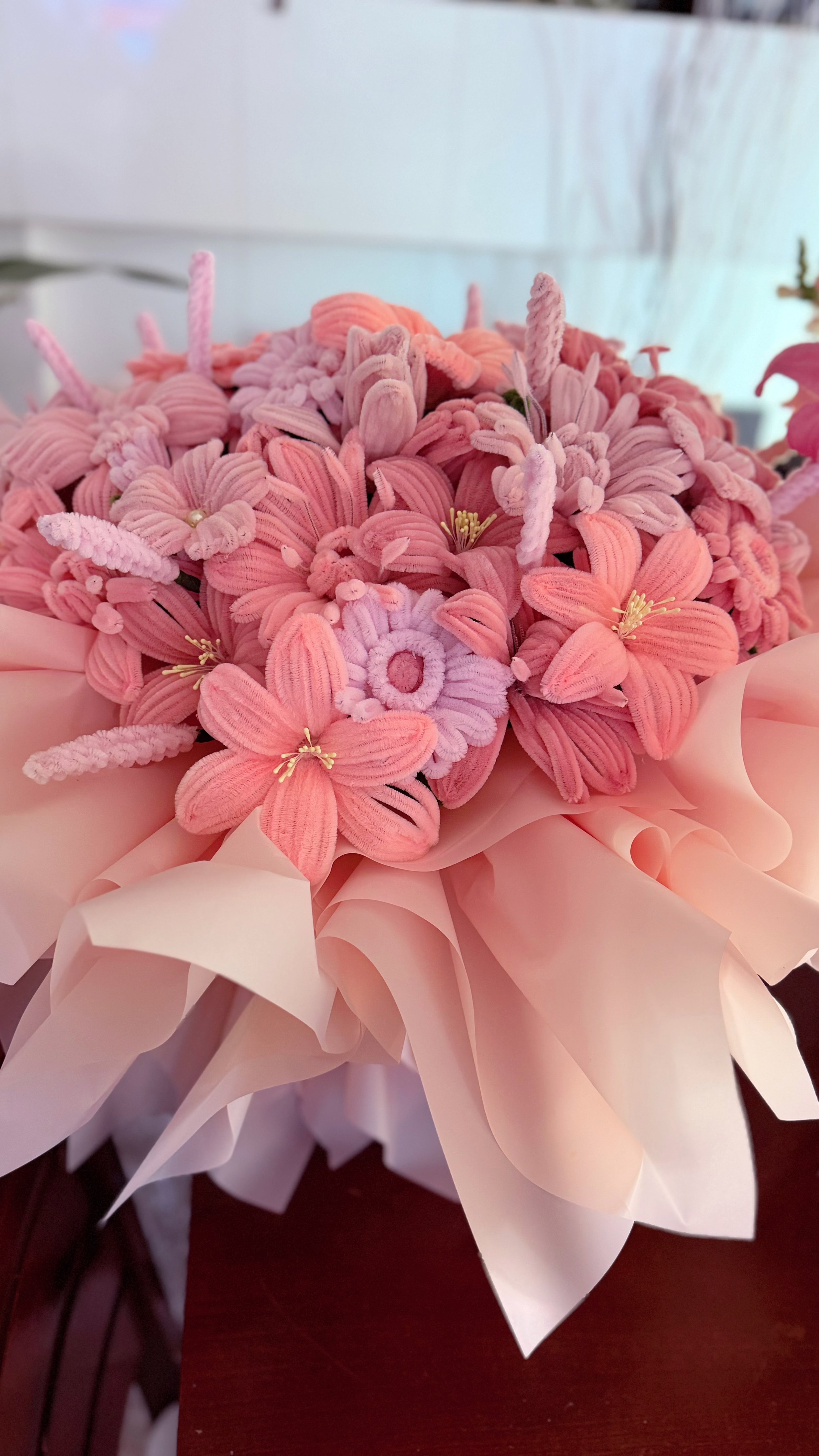 A bouquet of pink artificial flowers wrapped in light pink paper.