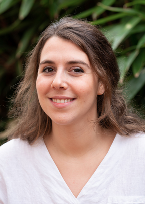 Photo of brown haired, brown eyed female doctor in front of  greenery