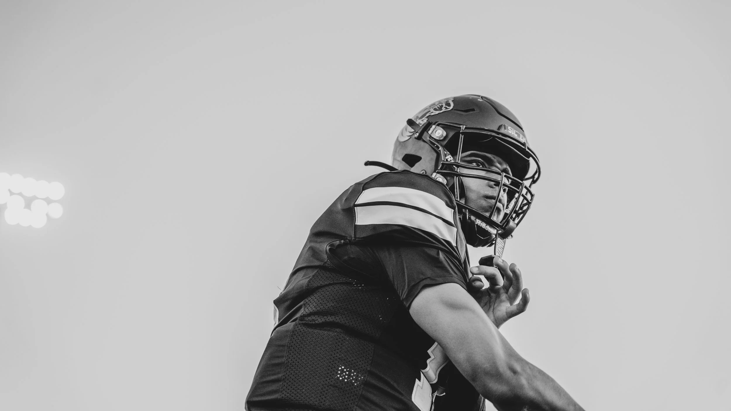 A football player wearing a helmet and uniform, looking to the side with a focused expression.