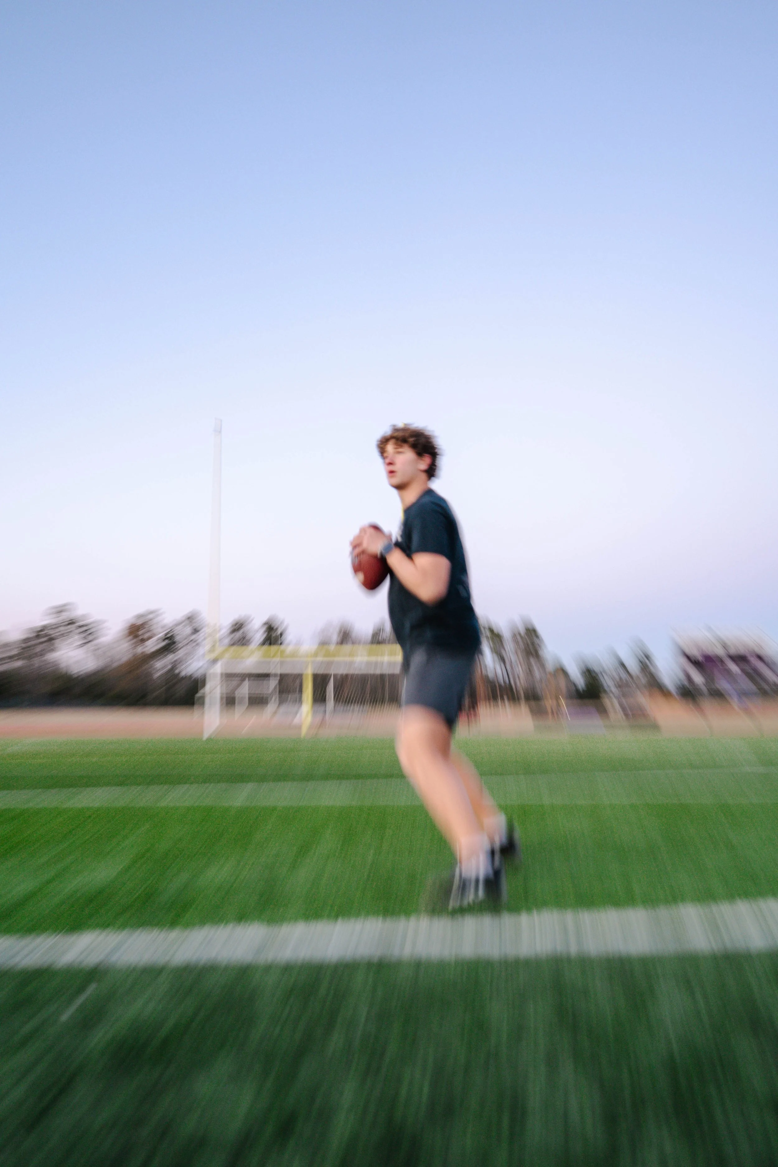 Young man holding a football on a sports field during evening with a clear sky