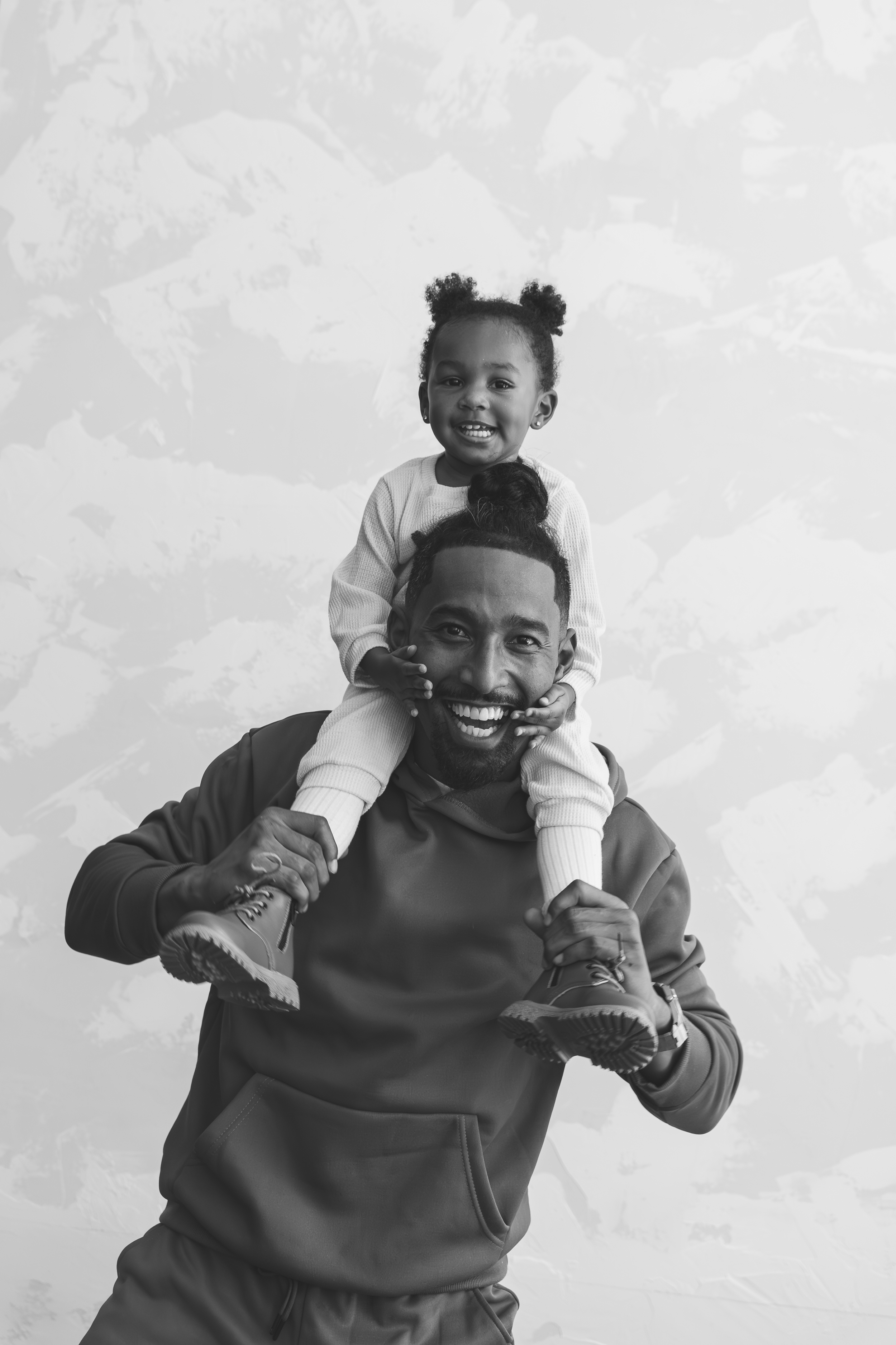 A man carrying a young girl on his shoulders, both smiling and looking at the camera, in black and white.