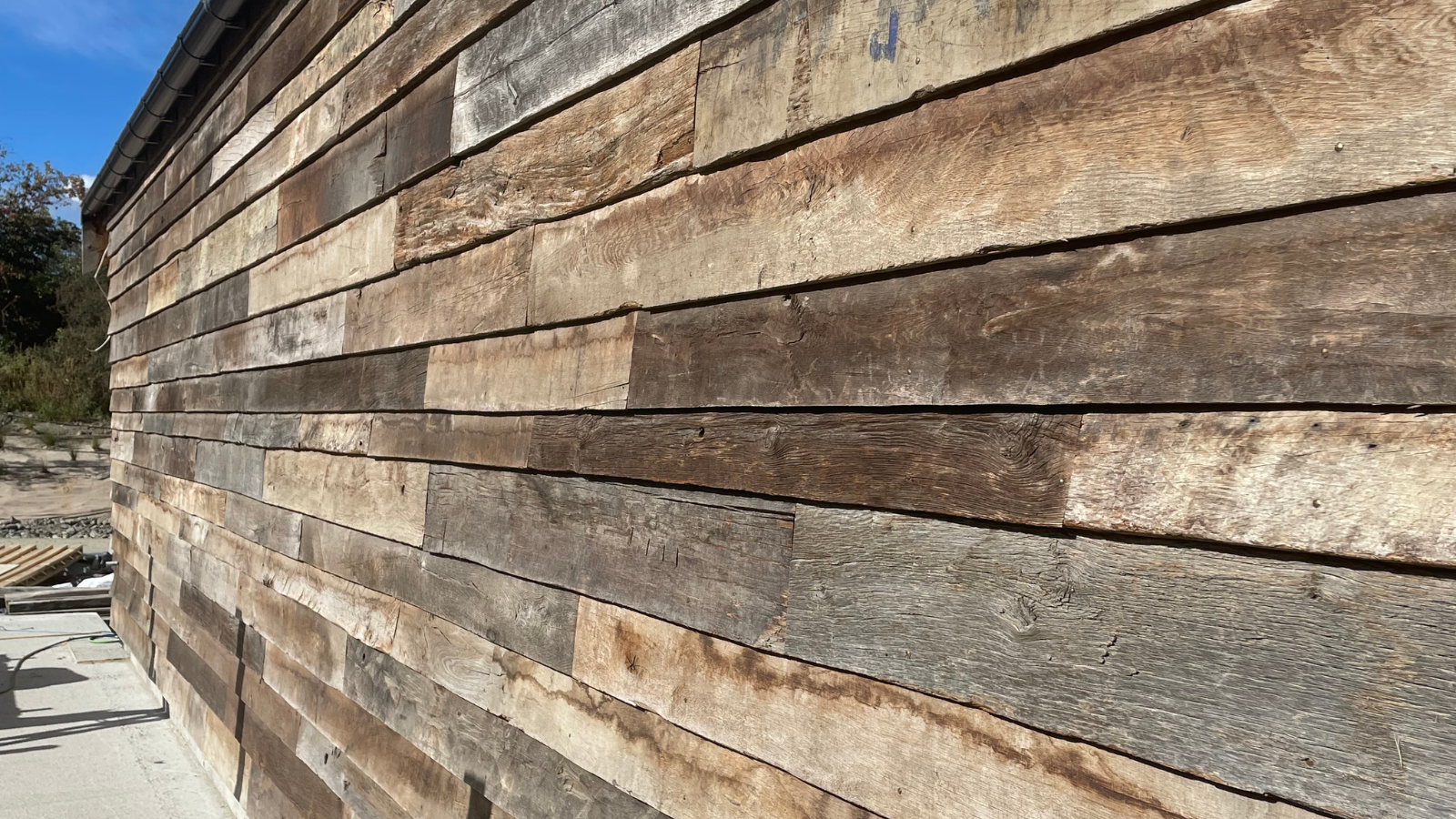 Close-up detail of reclaimed oak cladding boards showing weathered timber tones, aged surface texture and natural character.