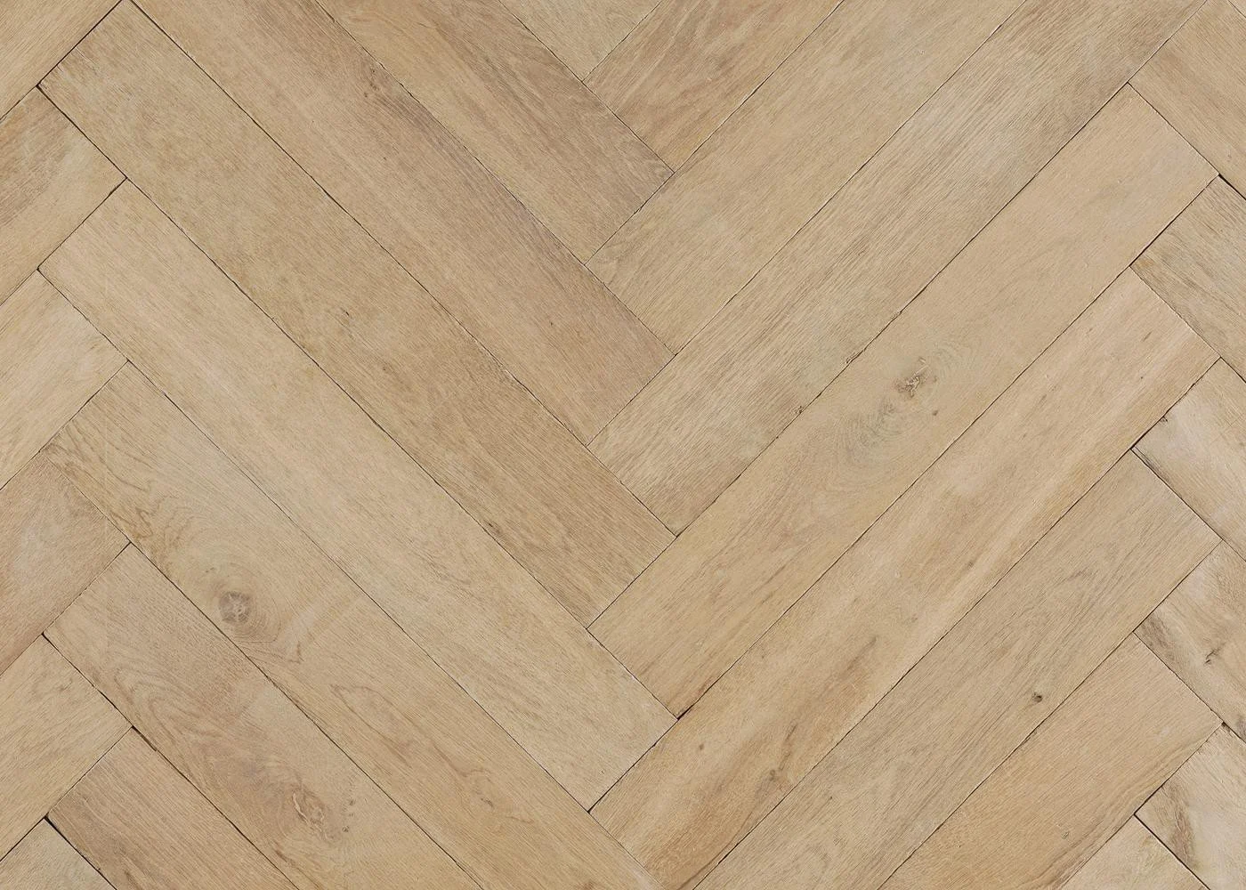 Close-up of pale oak herringbone flooring with a softly aged surface, natural grain and subtle tonal variation.