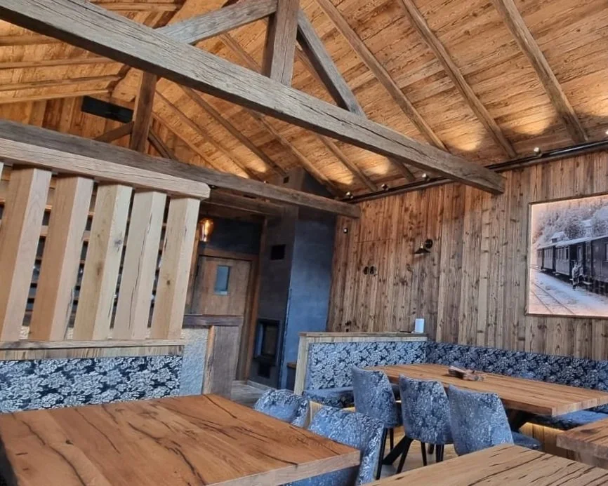 Interior of a rustic restaurant or cafe with wooden walls, ceiling, and furniture. There are wooden tables