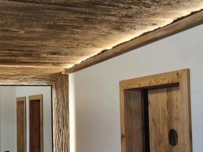 textured, rough wooden ceiling, a smooth white wall, and a wooden door 