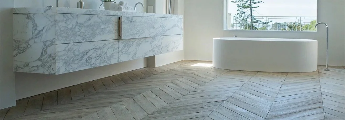 Oak chevron flooring in a light bathroom interior, adding warmth and natural texture alongside the stone bath surround.