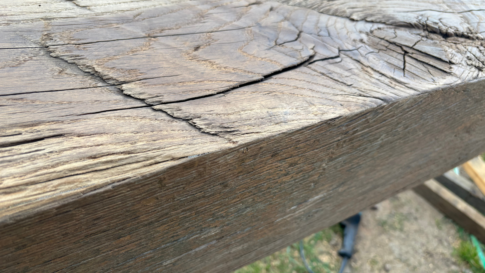 Close-up detail of a rustic reclaimed oak fireplace mantel with natural patina, aged grain, cracks and historic character.