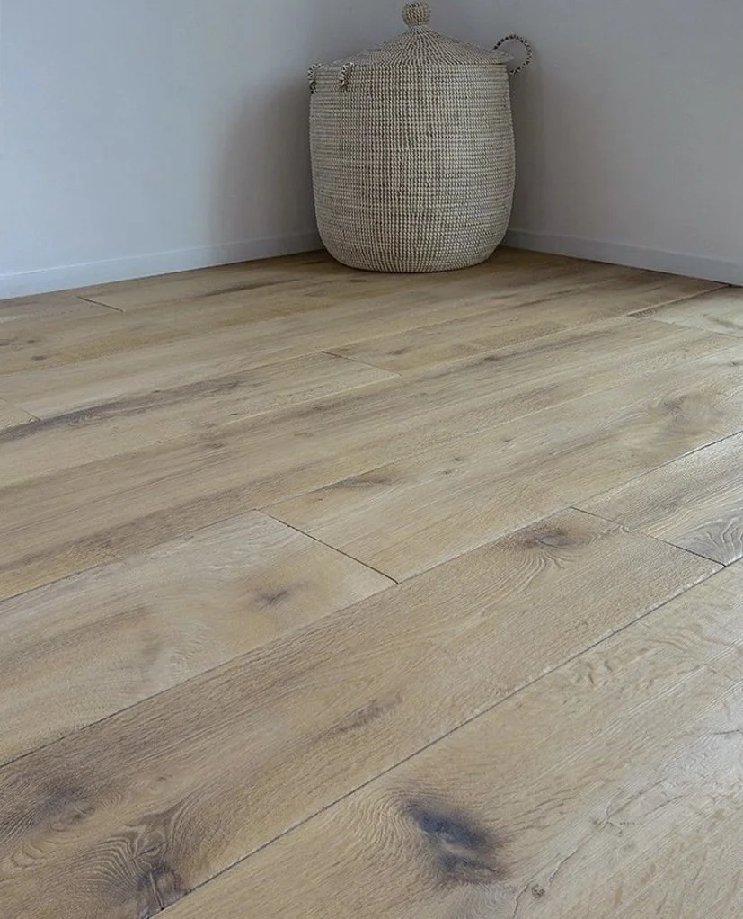 Close-up of a light wooden floor with a woven basket in the corner against a white wall.