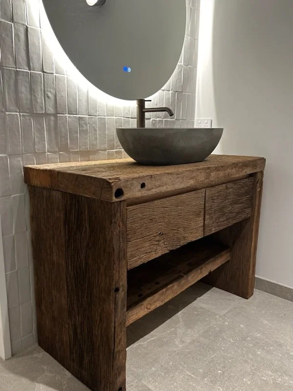 A rustic wooden oak bathroom vanity with a stone vessel sink.