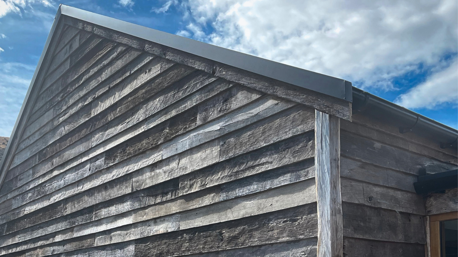 Reclaimed barn wood cladding installed across a residential gable, showing weathered grey tones, aged texture and natural board variation.