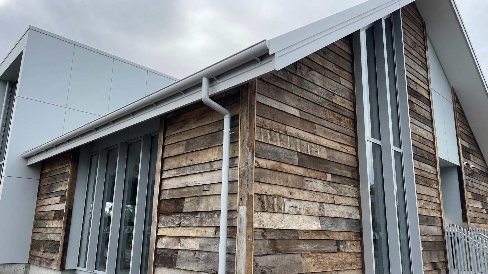 Reclaimed barn wood cladding installed on a contemporary building exterior beside tall windows and metal wall panels.