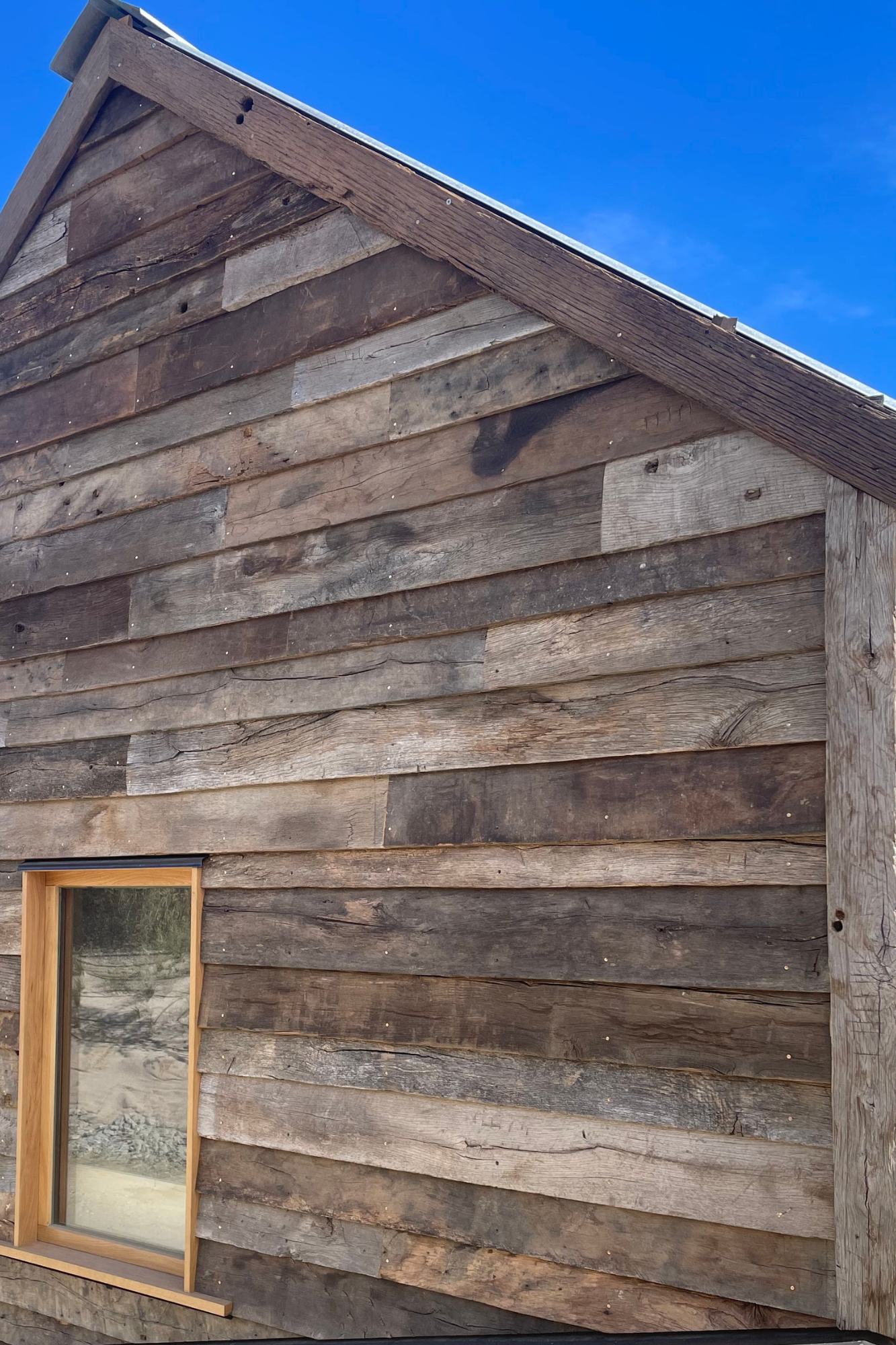 Reclaimed European oak boards used as exterior gable cladding with natural weathering, aged texture and tonal variation.