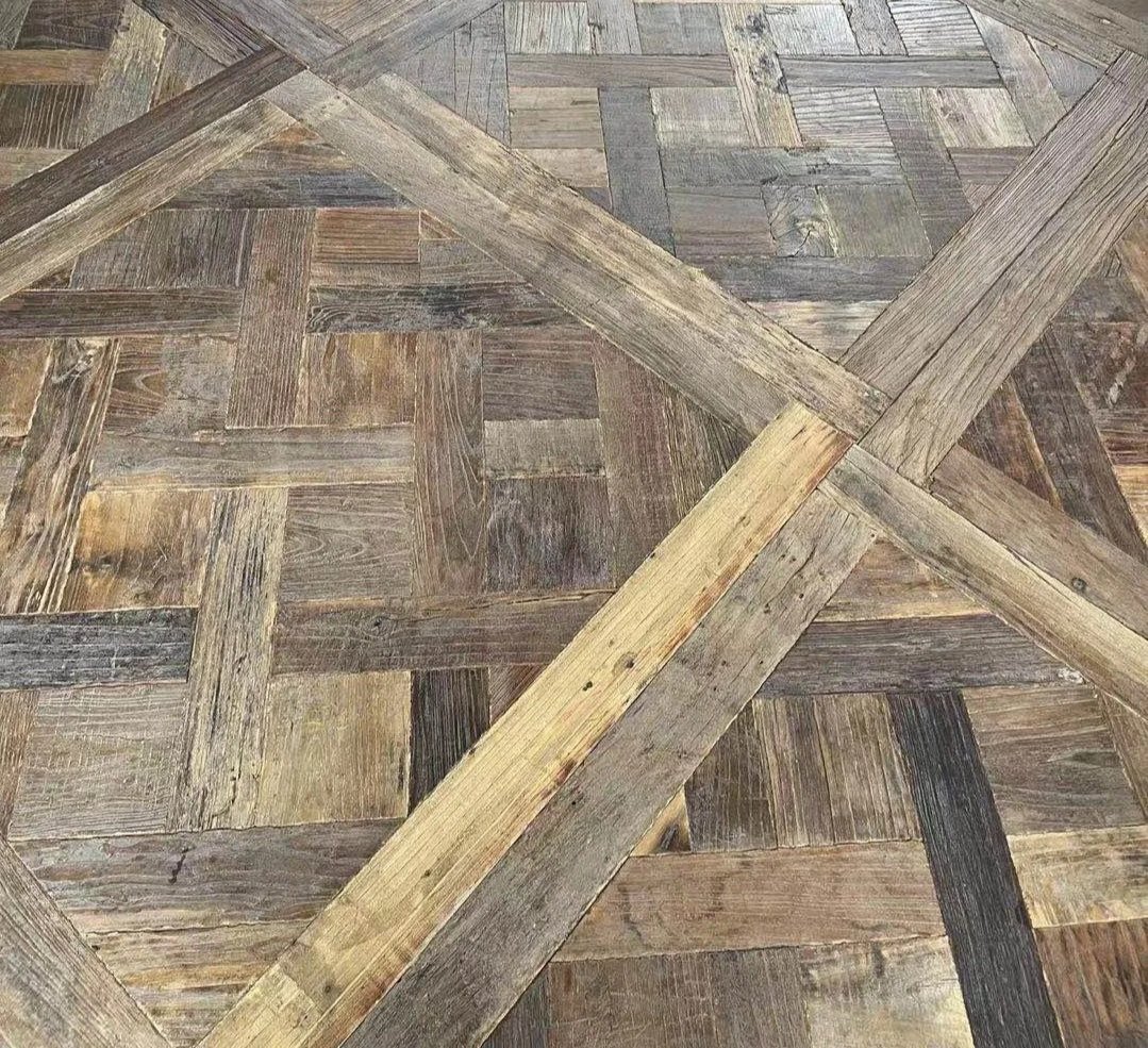 Close-up of a wooden parquet floor with various shades of brown and gray wood tiles arranged in a geometric pattern of squares and diagonal lines.